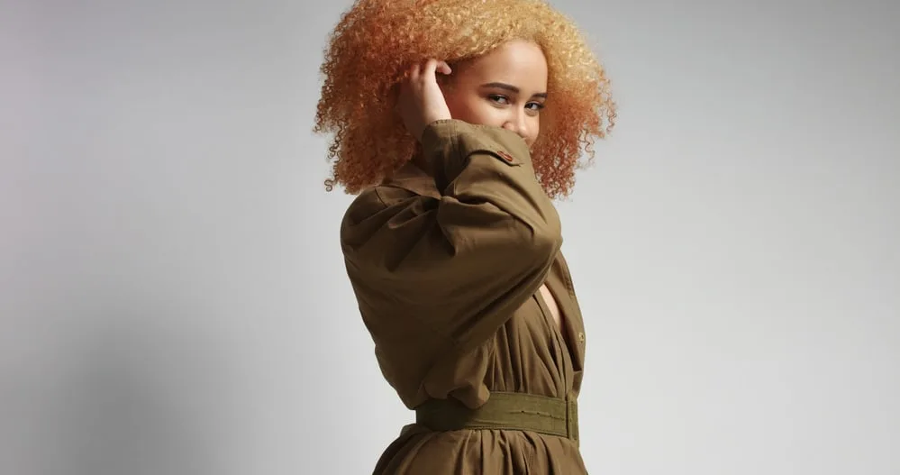 Lady rubbing her hair with a green khaki coat with a belt around her waist 