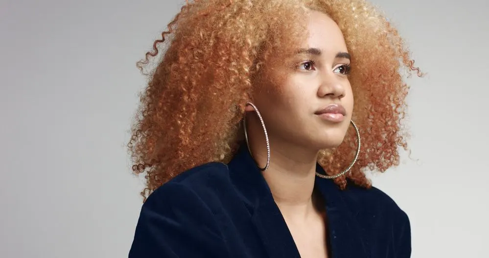 Black female with curly hair that been treated with bleach powder and liquid ammonia wearing a blue jacket