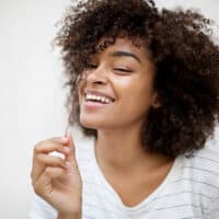 Beautiful young African American woman smiling at the camera with curly hair after using chebe powder for hair growth and length retention.