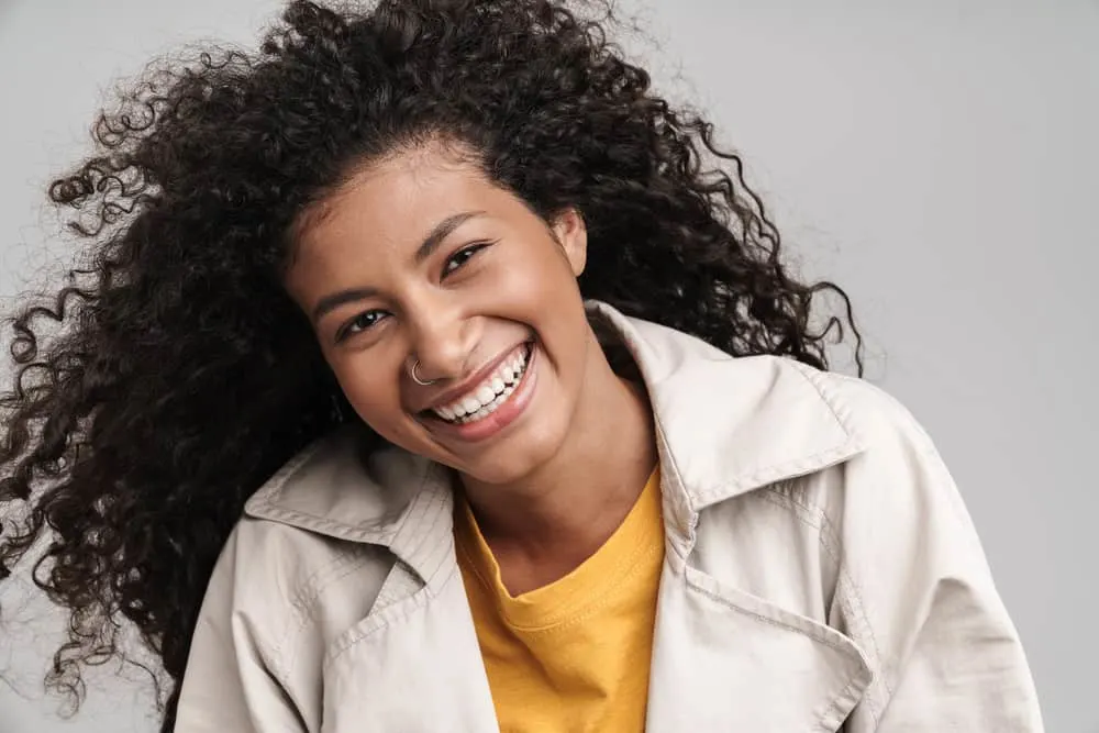 Cute black woman with a big smile and curly hair wearing a fall coat and an orange t-shirt. 