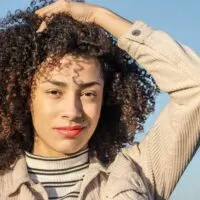 Young black girl with a pretty smile rubbing her fingers through her naturally curly hairdo that's been treated with cold-pressed rosehip oil.