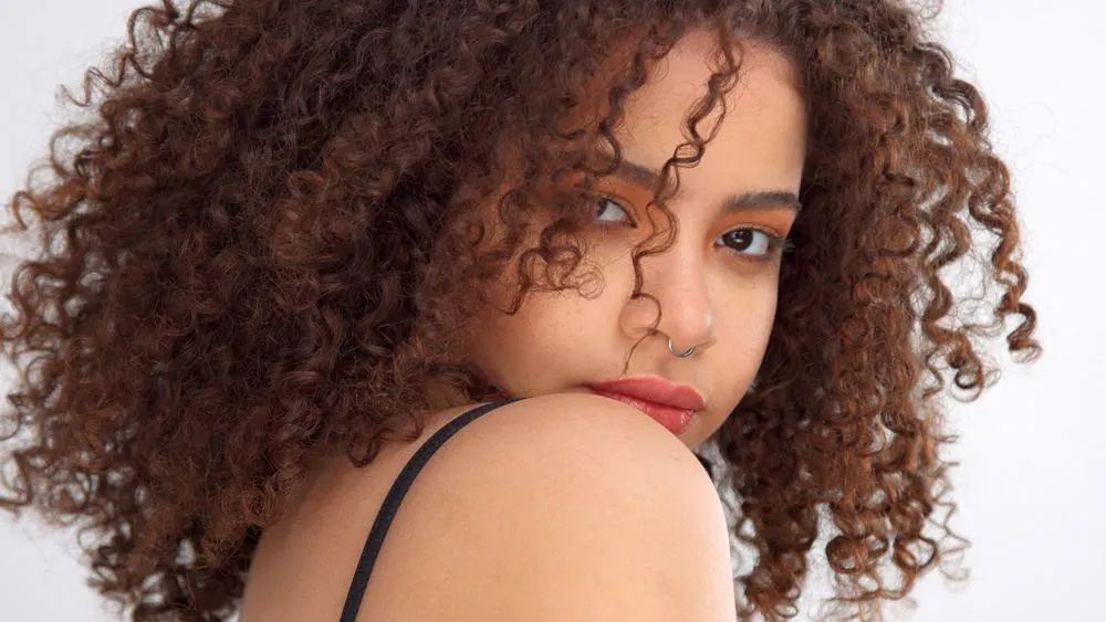 Black girl with nose ring with har natural curls covering parts of her face. 