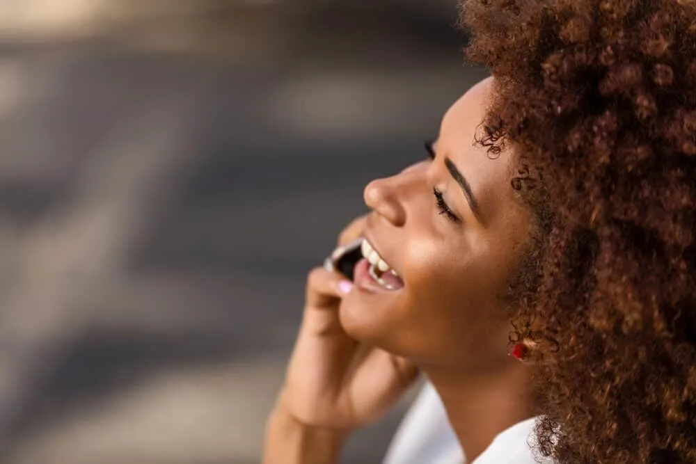 African American female with hair extensions treated by coconut oil sitting on a park bench.