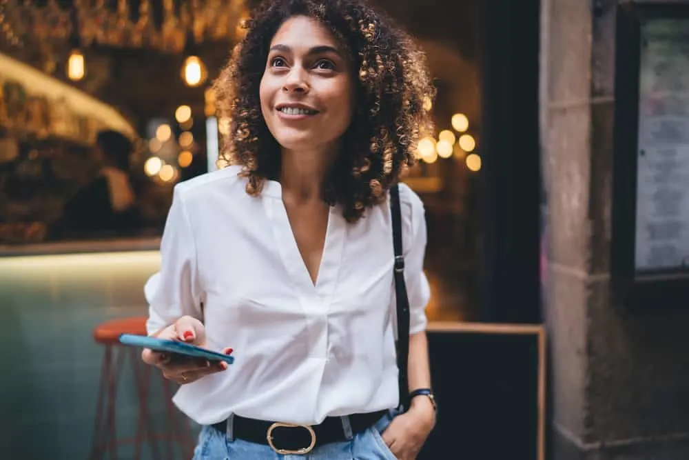 Beautiful black women wearing a white dress shirt, black purse, and blue jeans.