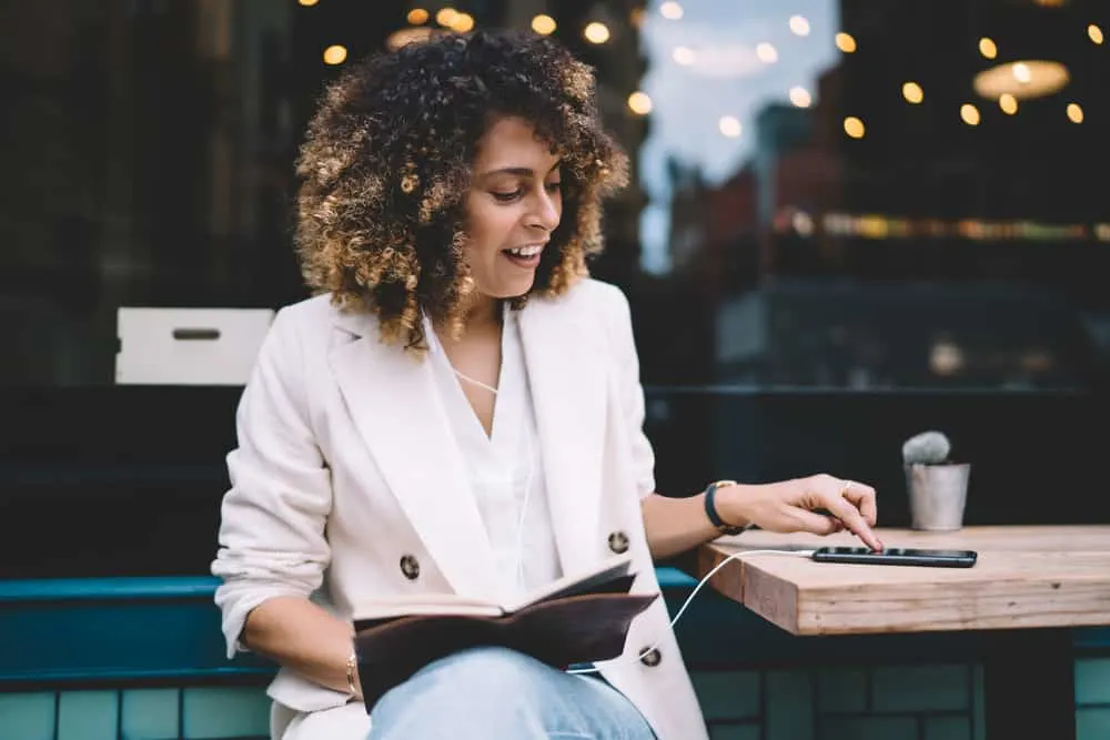 Women with type 3b natural hair wearing a stylish seersucker jacket and reading a book at a restaurant.