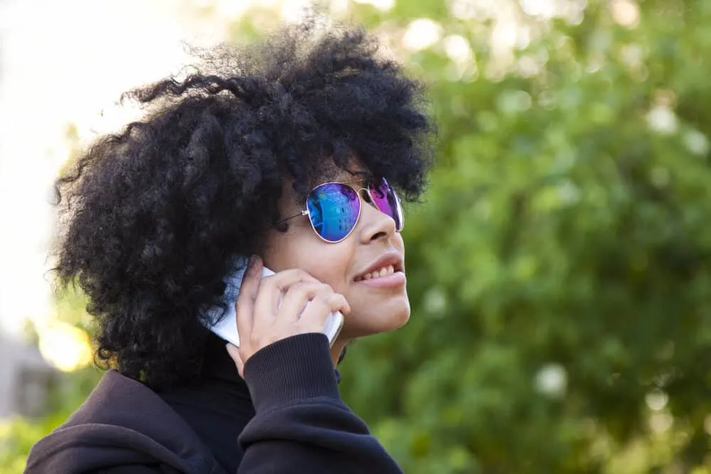 Black girl wearing a black sweatshirt and shades walking through the park on a fall day.