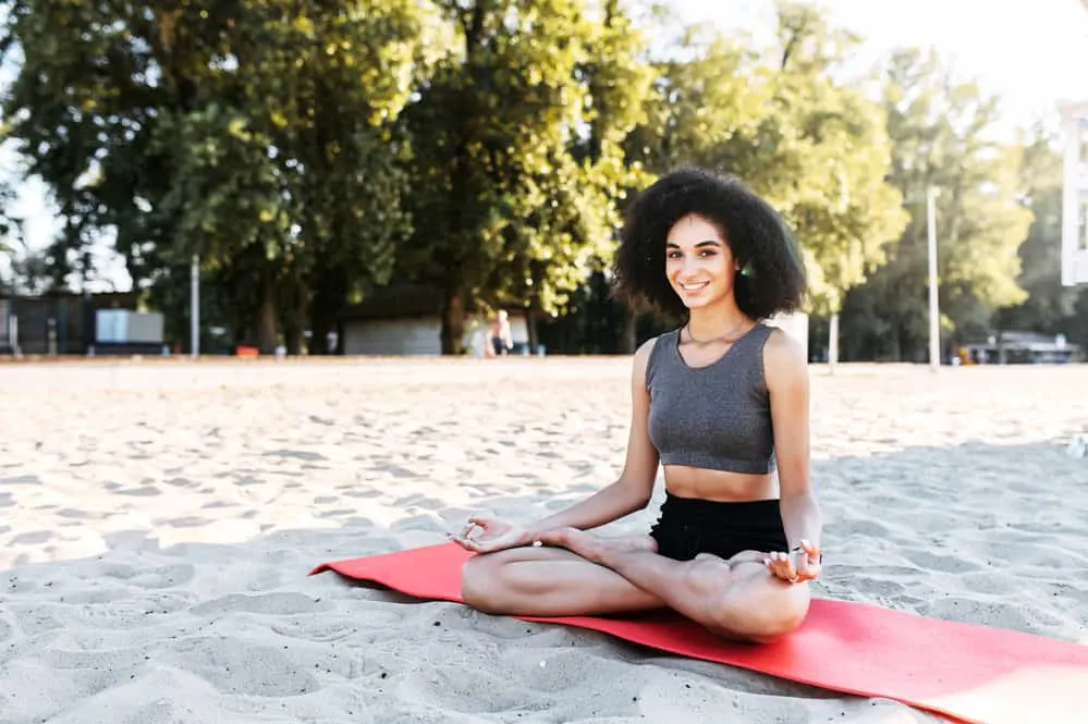 Attractive young woman practicing yoga in lotus pose on the beach with an afro hairstyle.