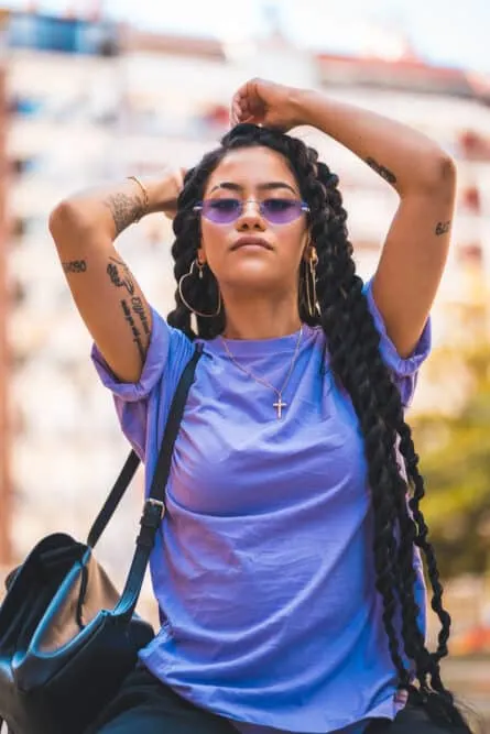 Adult female wearing heart earrings, a Jesus Christ necklace, purple shades, and a black leather purse