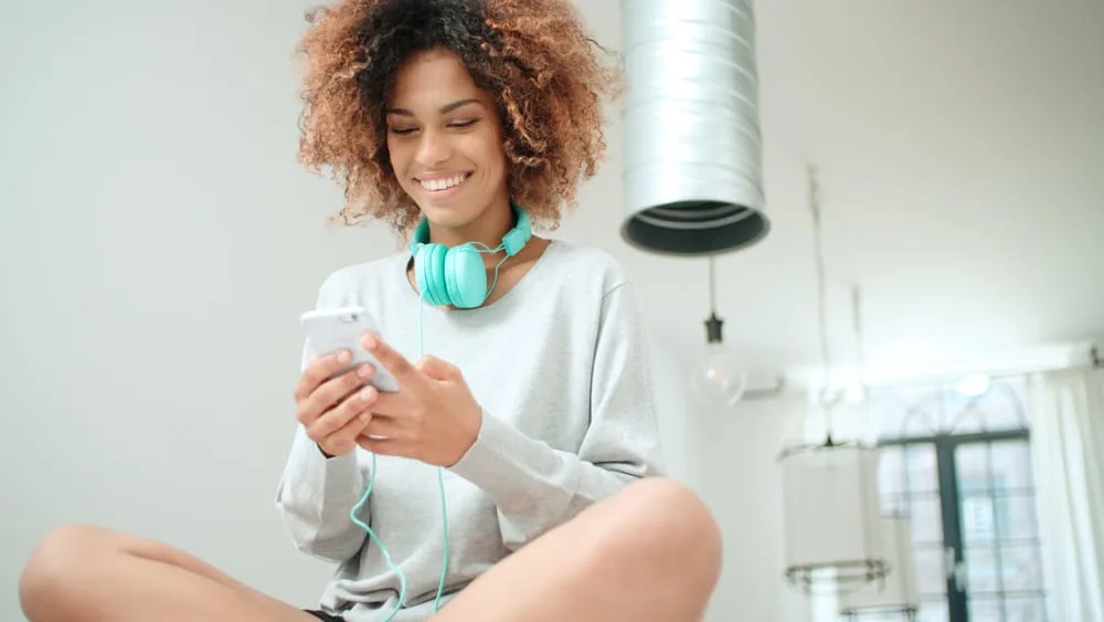 Woman with brown and black 4c natural curls sitting on the kitchen counter using her mobile phone