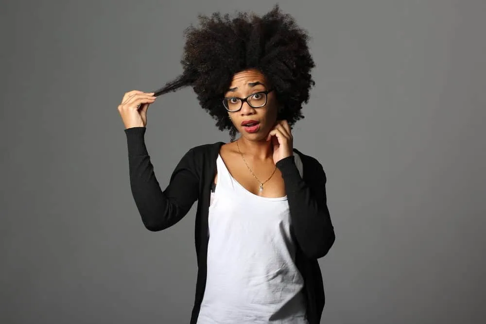 African American lady with 4C coils wearing black pearl earrings, a silver necklace, white t-shirt, and a black knit sweater.