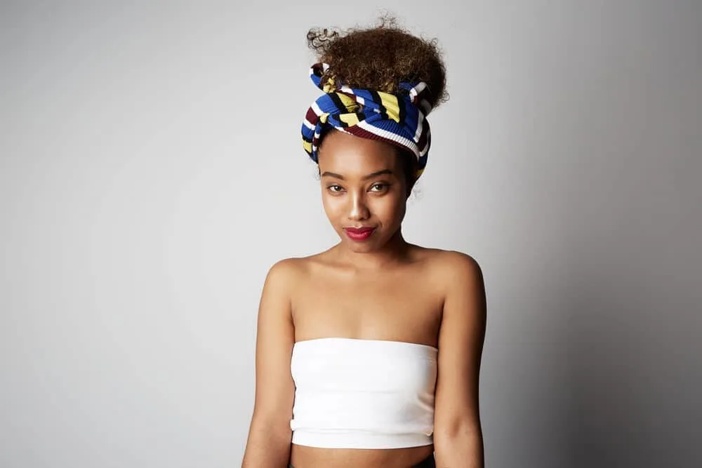 A young black girl talking a selfie after bleaching hair is wearing an African scarf over her hair, a white shirt, and red lipstick.