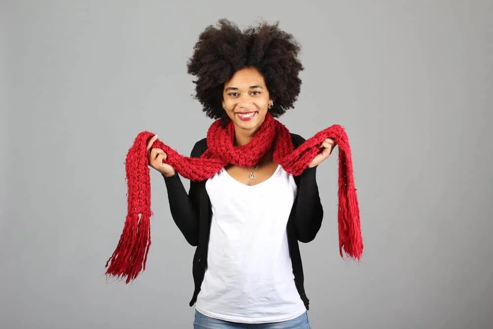 African American female wearing black pearl earrings, a silver necklace, red scarf, white t-shirt, and a black sweater.