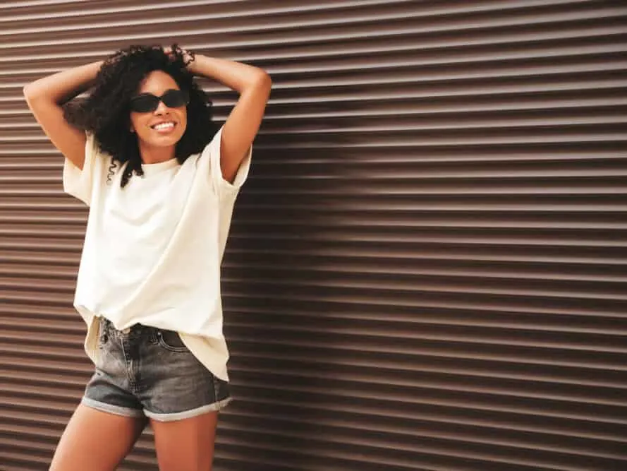 African American women with virgin hair wearing a white t-shirt, blue jean shorts, and loose curls.