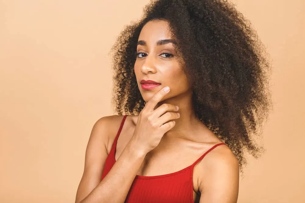 A black girl wearing a red shirt, bright red lipstick, and purple nail polish.