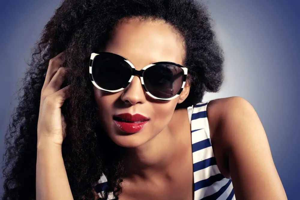 Black girl wearing black and white sunglasses, red lips, and braiding hair attached to her regular hair.