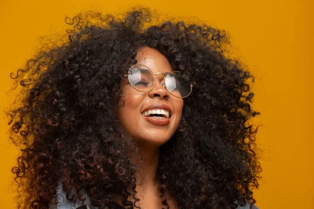 Black girl wearing weft extensions lengthening super short hair while also wearing glasses, red lipstick, and a blue jean shirt.