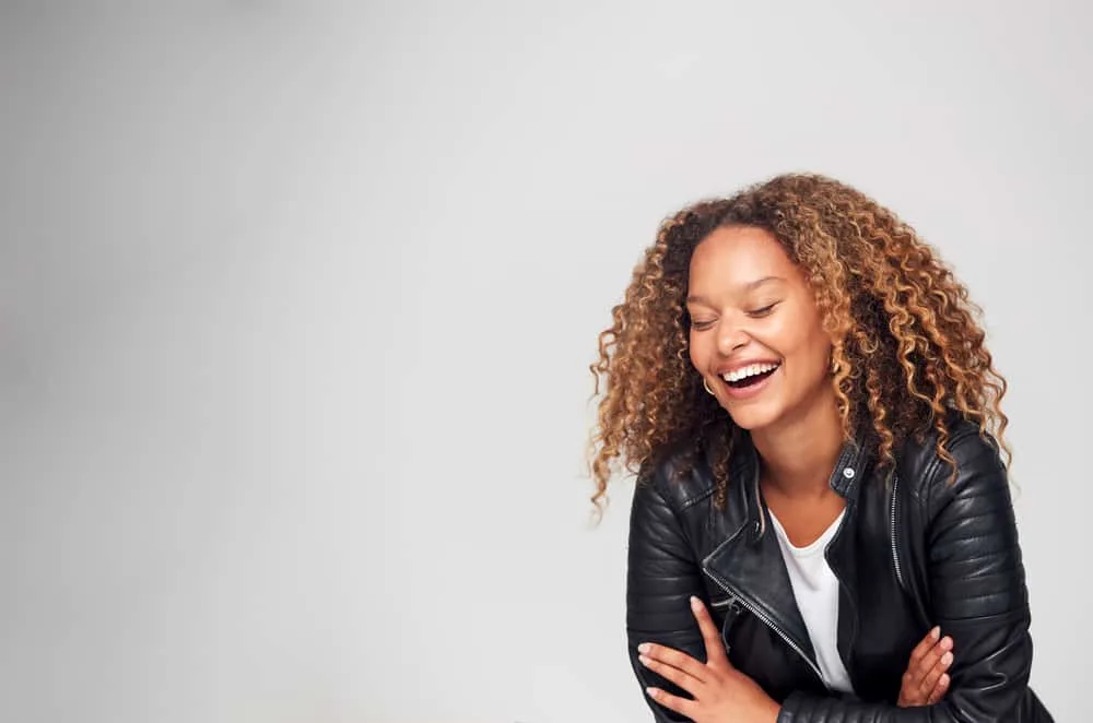 Women laughing with her eyes closed wearing a curly brown hairstyle.