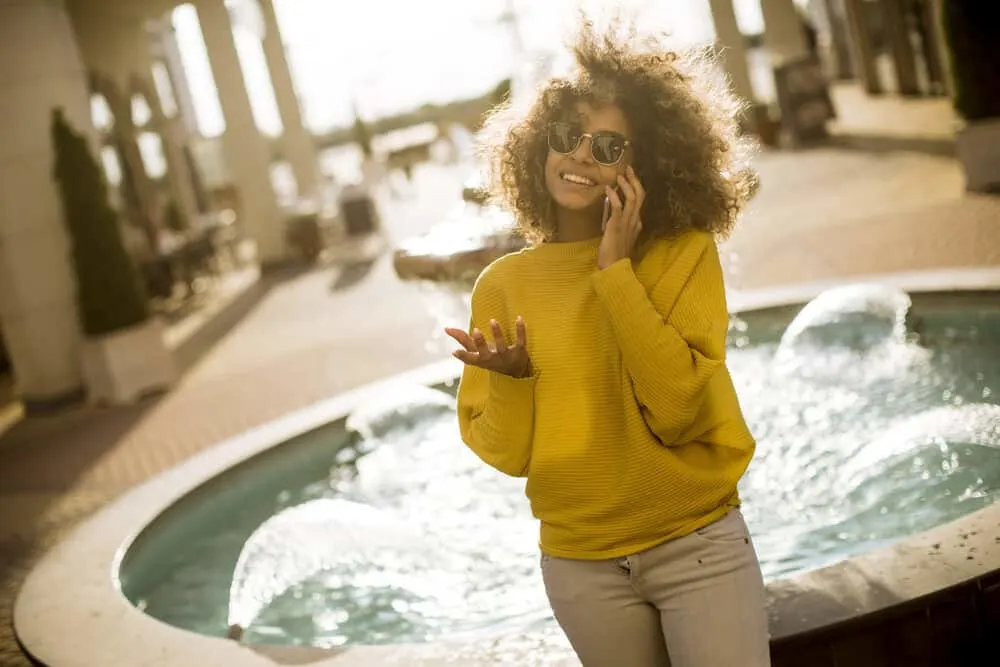 Attractive young woman with a light auburn natural color on virgin hair chatting on her cell phone about her hi-color highlights.