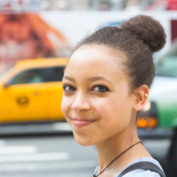 A black girl with dyed hair, blue eye shadow, and a great smile used a lice comb to treat lice instead of chemicals.