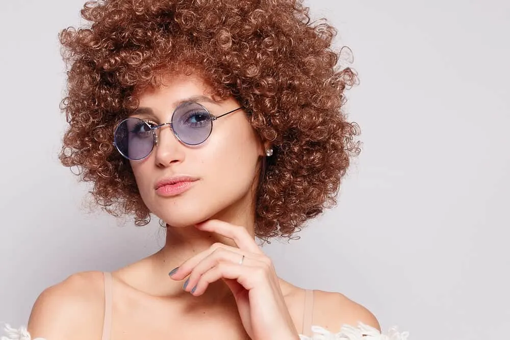 Beautiful lady with light brown brassy hair and a pale yellow skin tone wearing blue-tinted glasses and diamond earrings