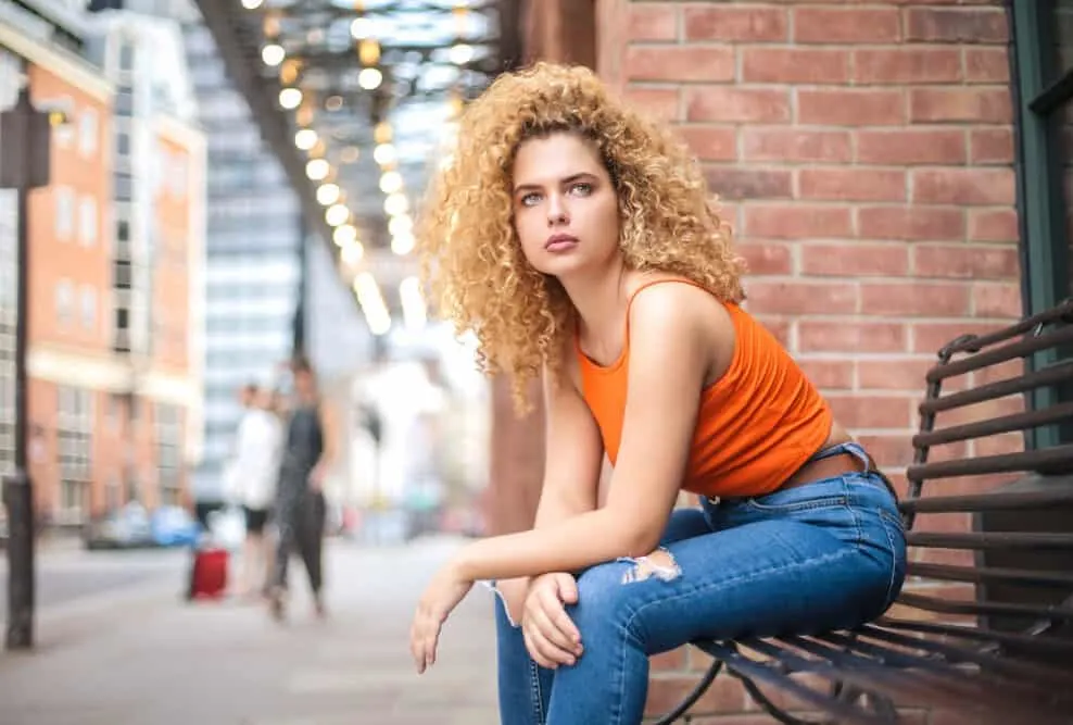 White adult female sitting outside a bench with dark blonde hair with warm undertones