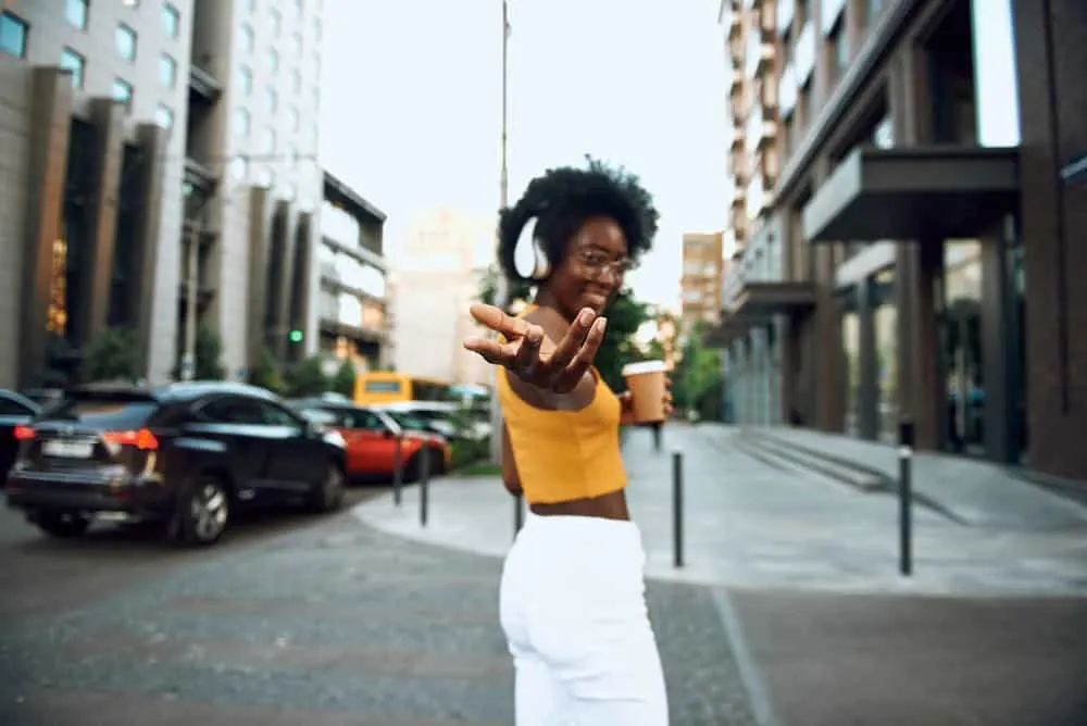 Cute black girl with naturally wavy hair wearing a yellow shirt and white pants.