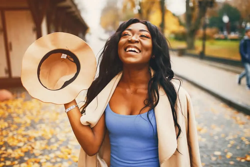 Lady outside with straight hair on a fall day smiling as the wind blows leaves around her