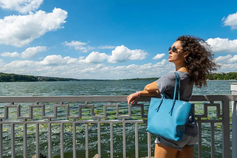 White girl with brown and black hair strands wearing sunscreen near the lake.