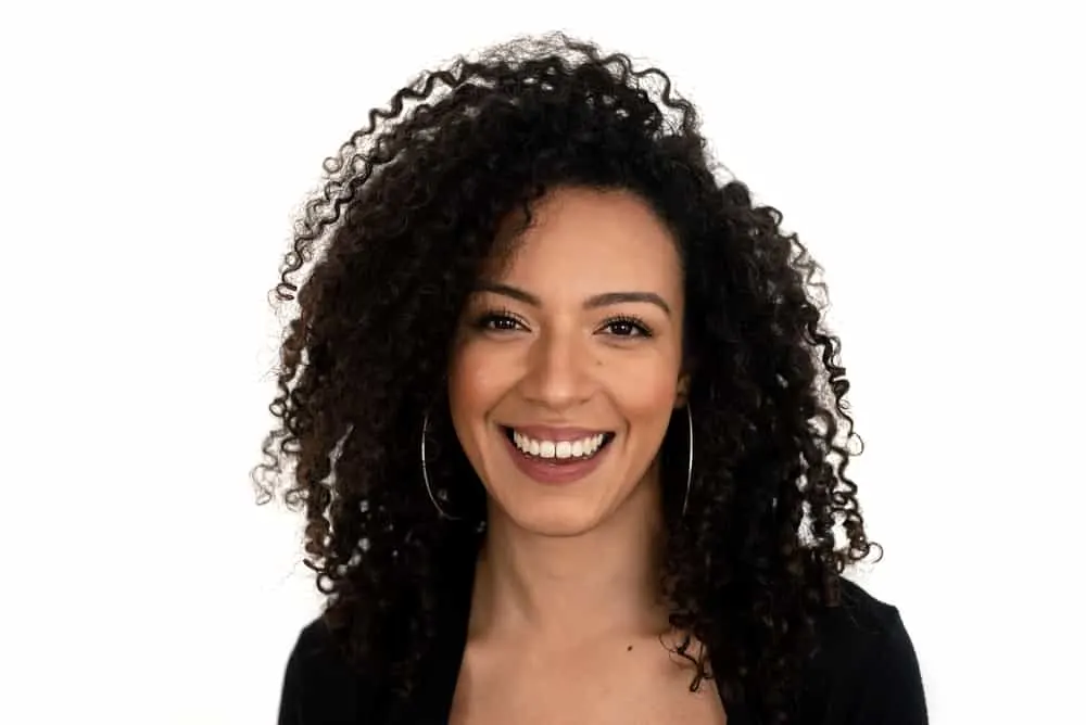 Cute female starting her natural hair journey with bouncy curls wearing hoop earrings and wavy curls.