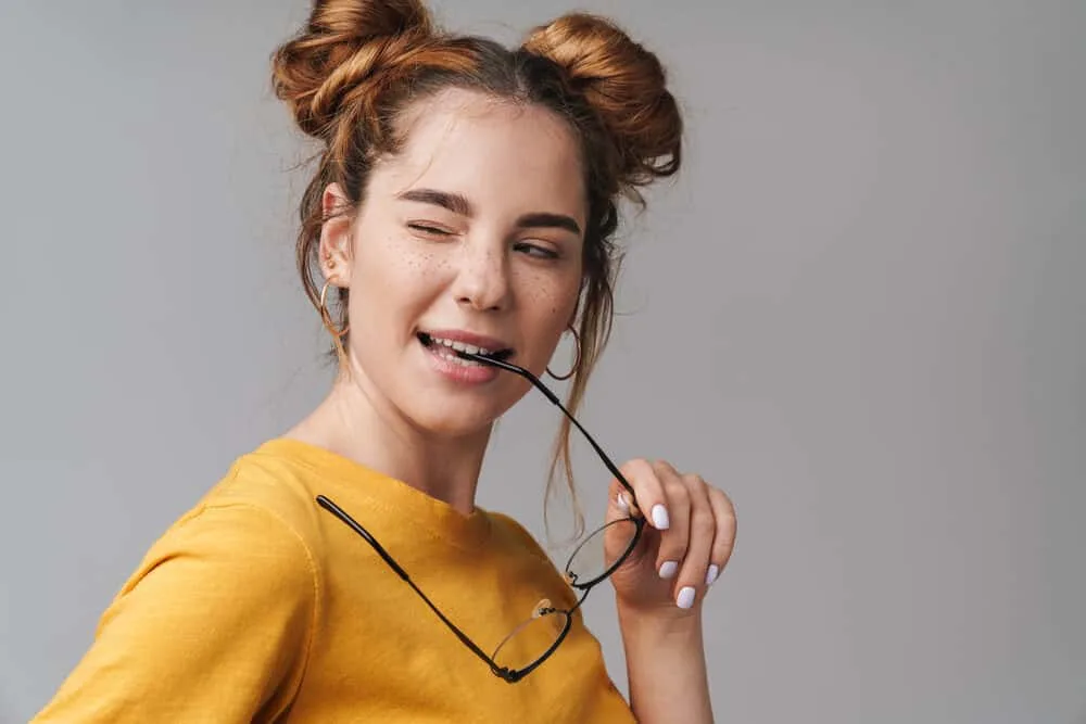 White girl winking while wearing an orange shirt and gold hoop earrings