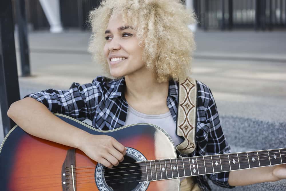 Fröhliche Frau mit dunkel gebleichtem Haar, die beim Gitarrenspielen in die Menge lächelt