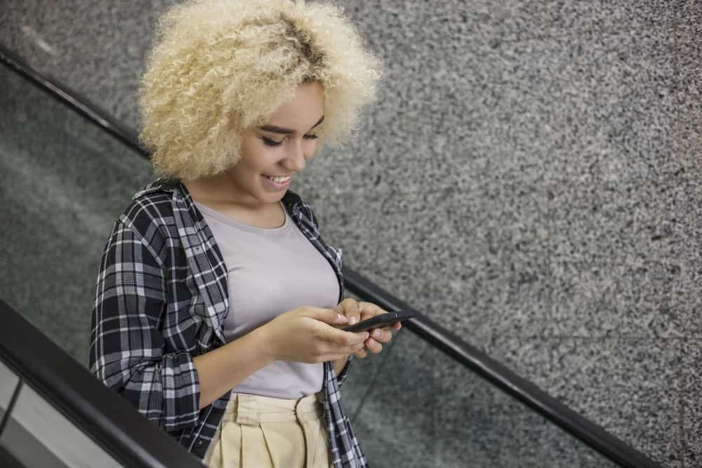 Hermosa mujer afroamericana en el centro comercial con cabello amarillo tonificado con champú morado en una escalera mecánica 