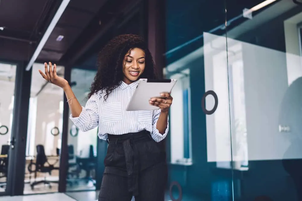 Black lady using a tablet while wearing a blue and white shirt and black pants