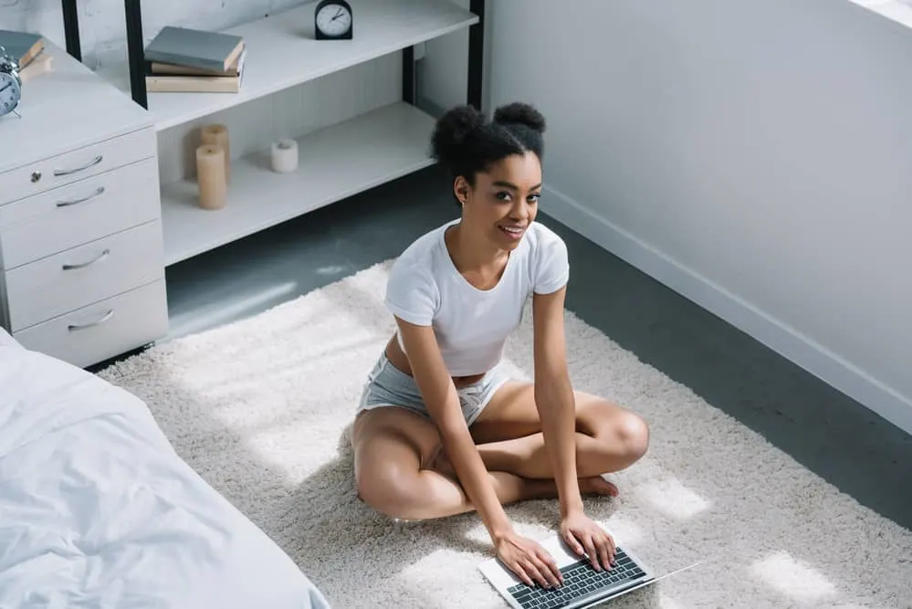 Beautiful black woman using her computer on the bedroom floor