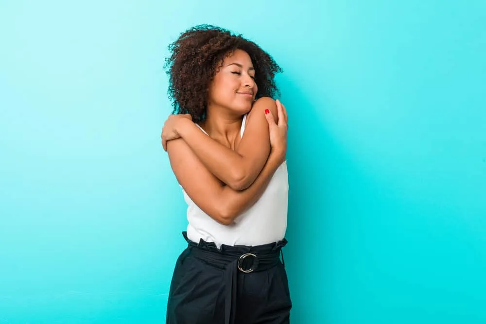 Black girl with passion twists hugging herself with her eyes closed