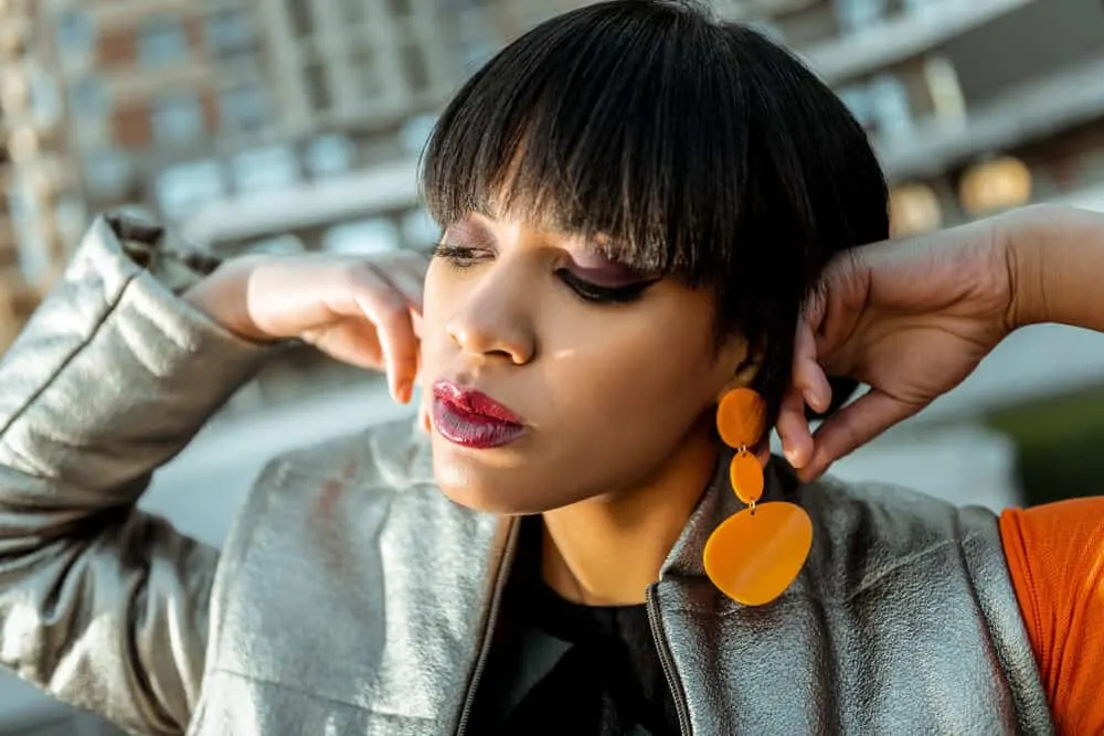 Dark-haired lady with a bad haircut with existing layers wearing orange plastic earrings 