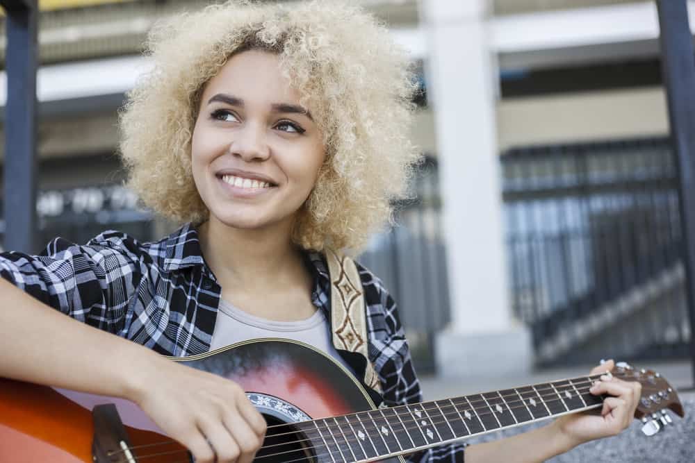 afroamerikansk pige med askeblond hårfarve spiller guitar udenfor