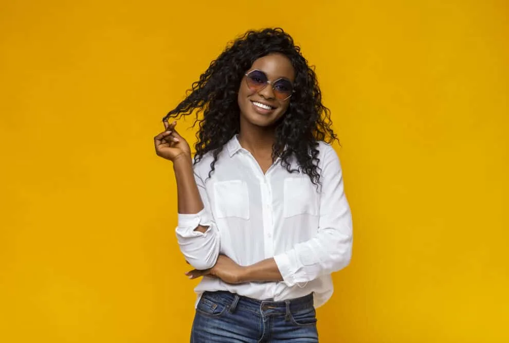 Female wearing sunglasses, a white shirt, and jeans with a wavy virgin hair bundle 