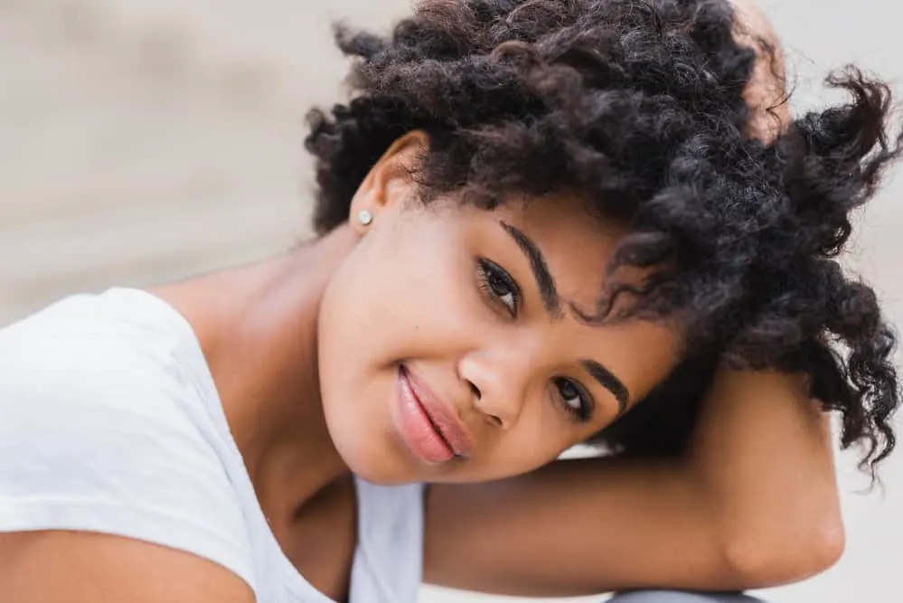 Cute African American female with curly hair treated with essential oil after washing with a gentle shampoo