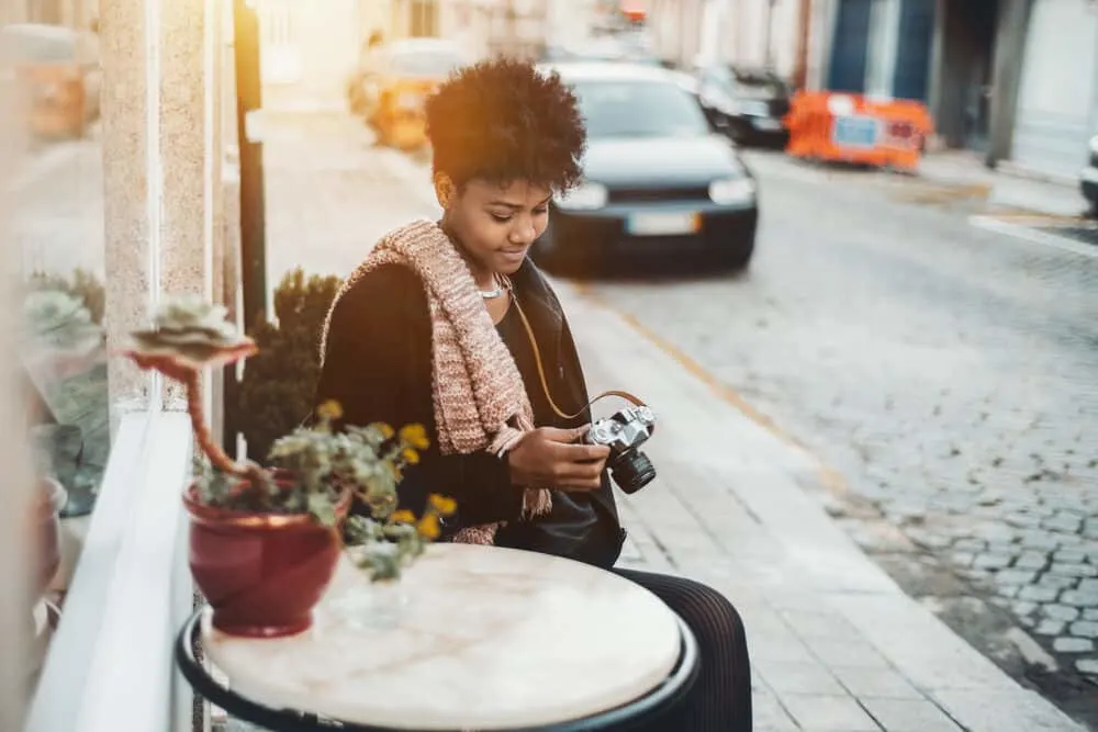 Cute Brazilian curly girl sitting outside a restaurant using a camera