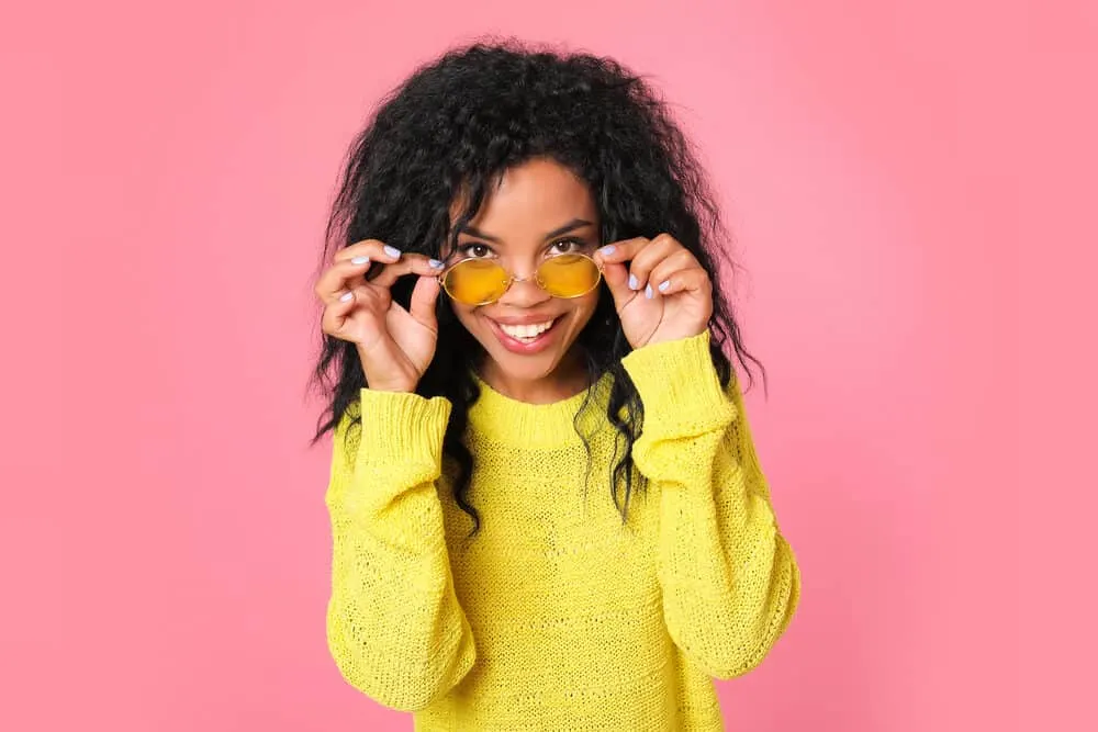 Light-skinned girl with human extensions wearing sunglasses and a yellow sweater