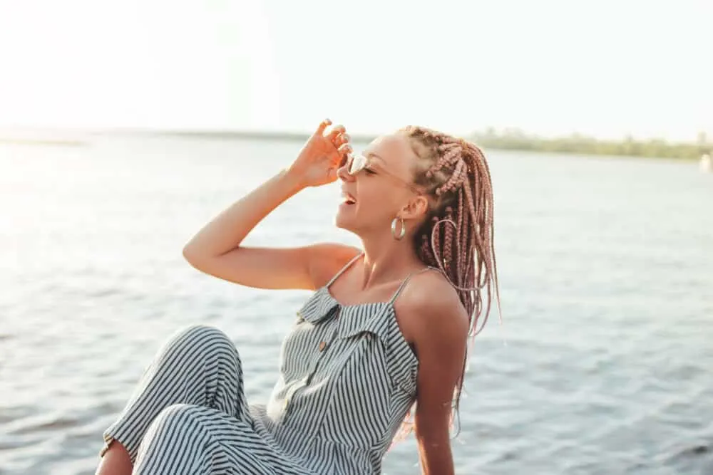 A white lady sitting on the beach with her hair braided in thick braids