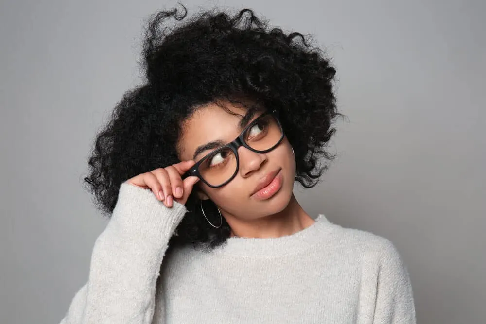 Black lady wearing glasses, pink lipstick, and a gray sweater. 