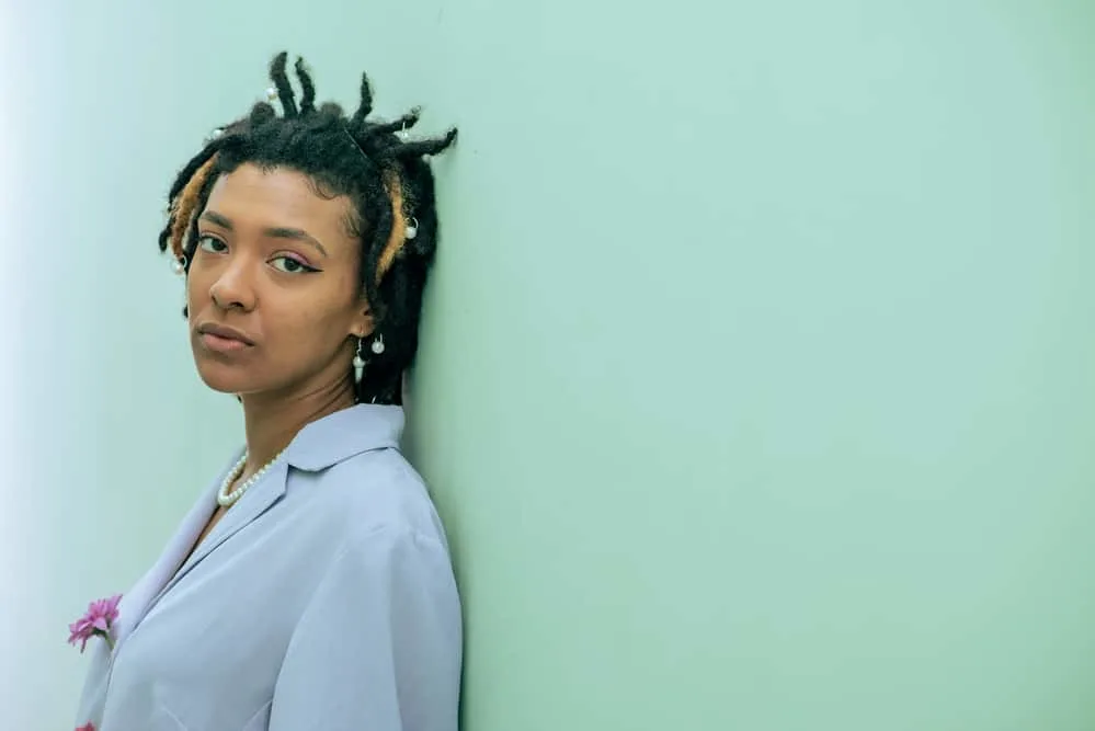 A beautiful young woman leaning against a green wall with starter locs