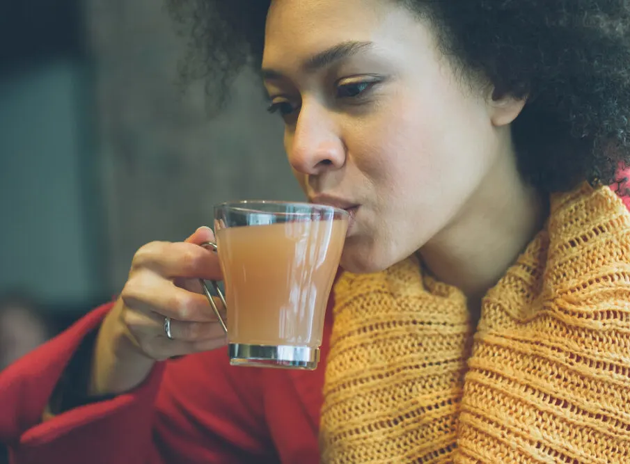 Cute black lady with tea bag in hot water wearing a read jacket on a cold winter day.