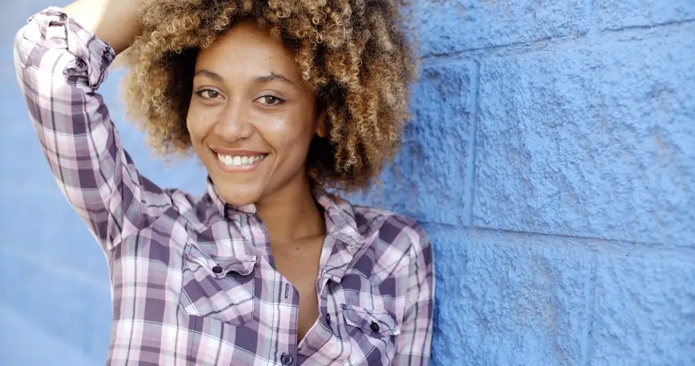 Cute black girl biting her lip with naturally brown hair with blonde highlights following a bleach bath lift.