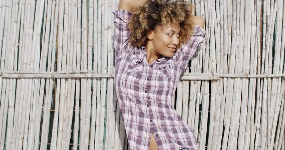 Girl with a fun pose in front of a reed wall with dark hair wearing a purple plaid dress shirt.