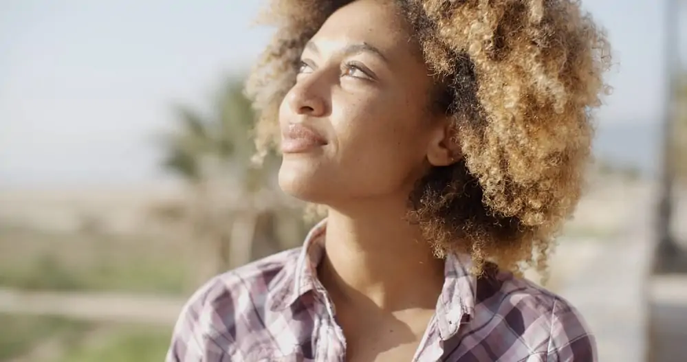 Young African woman on a sunny day with her 4C hair dyed blonde with medium brown undertones.