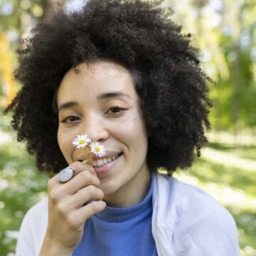 Mixed black girl with smooth skin and coarse hair smelling daisies outdoors