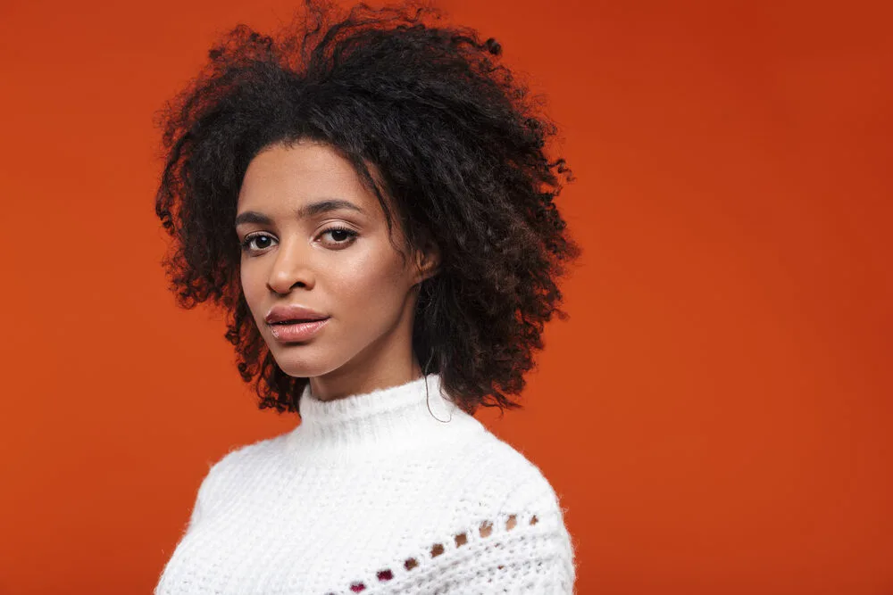 Young black lady with a cute smile wearing a white winter sweater on a cold day.